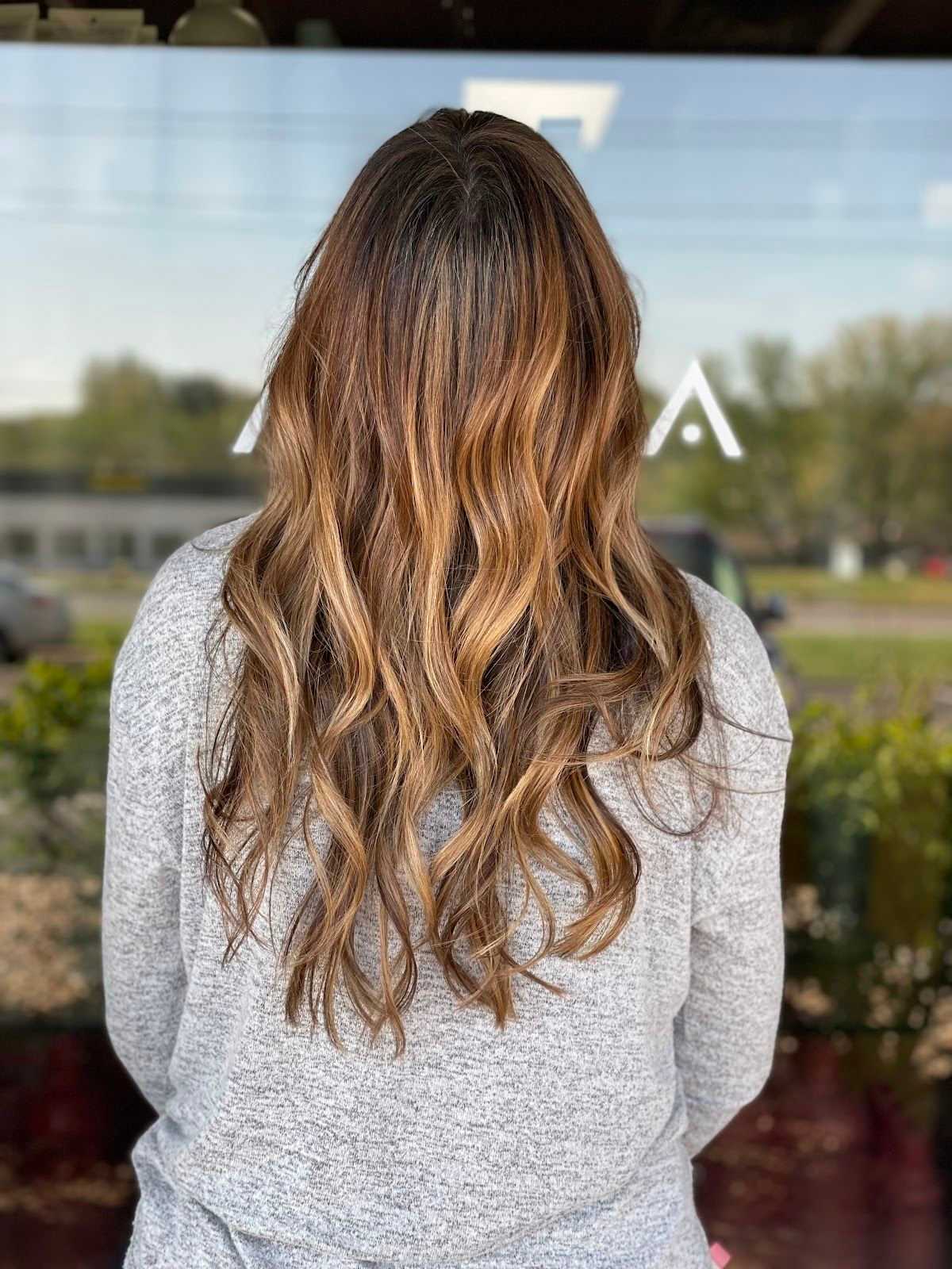 Woman with long, wavy, light brown hair in a grey sweater standing outdoors.